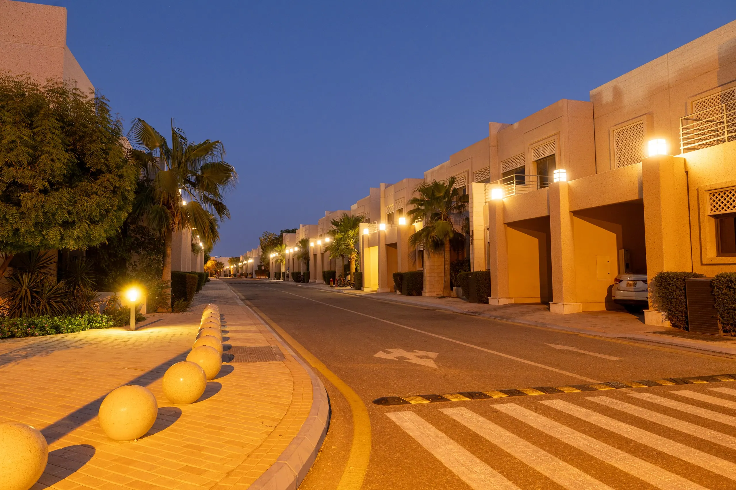 شارع فلل عند الغسق، وأعمدة حجرية وأضواء الواجهات تتوهج